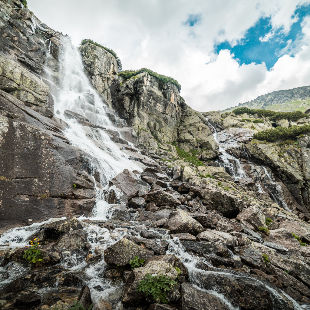 Водопад стекает по камням на фоне неба с белыми облаками