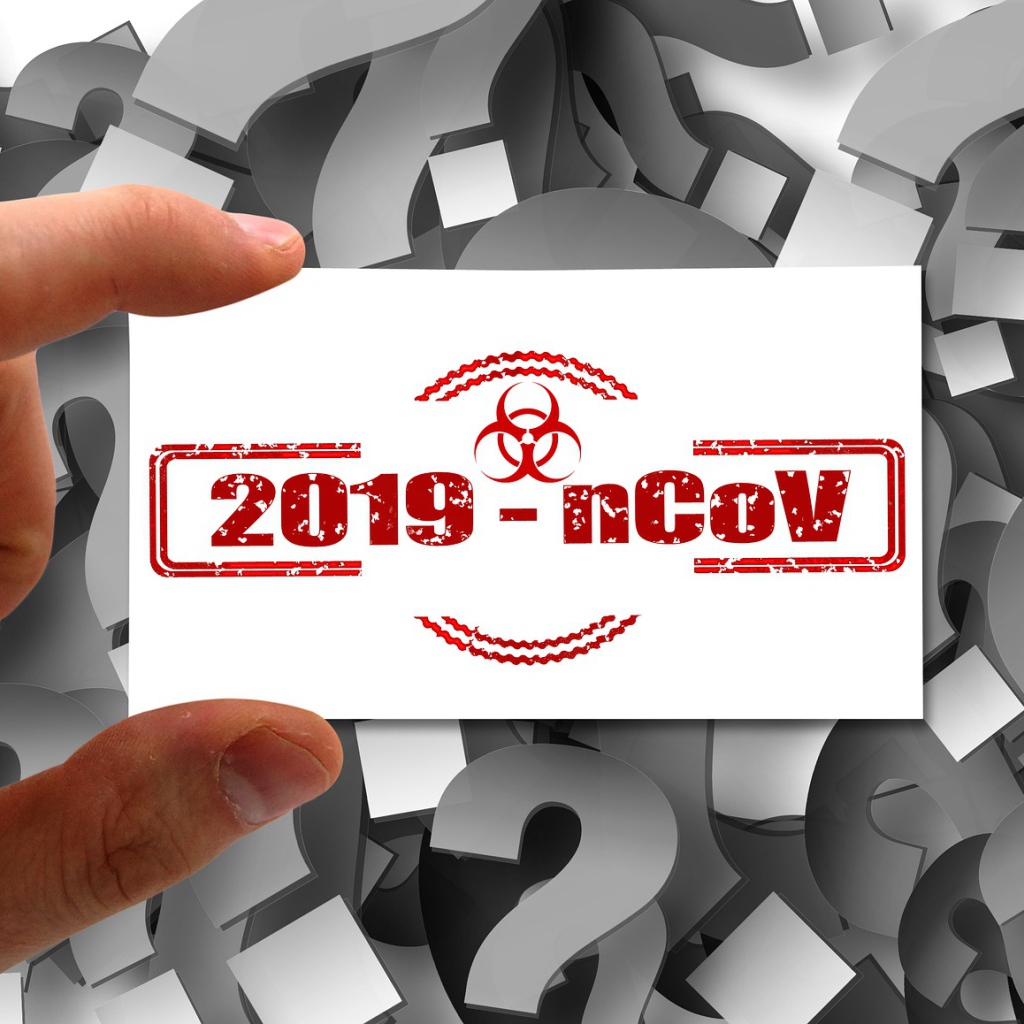 Табличка коронавирус covid-19 в руке на фоне знаков вопроса