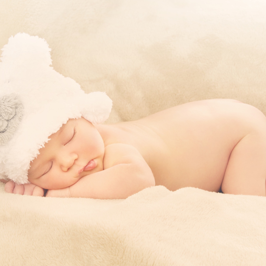 Грудной ребенок с белой шапке спит на кровати