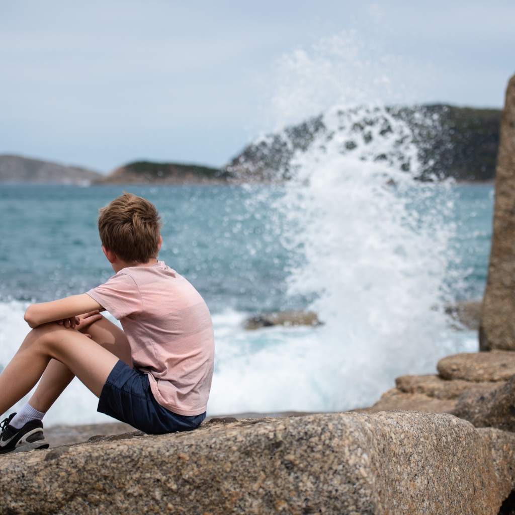 Мальчик сидит на камнях у бушующего моря