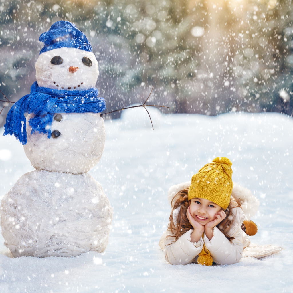 Милая девочка лежит на снегу у снеговика зимой