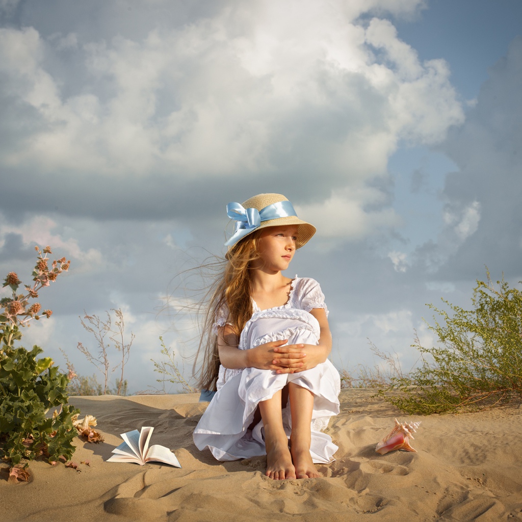 Красивая девочка в белом платье сидит на песку