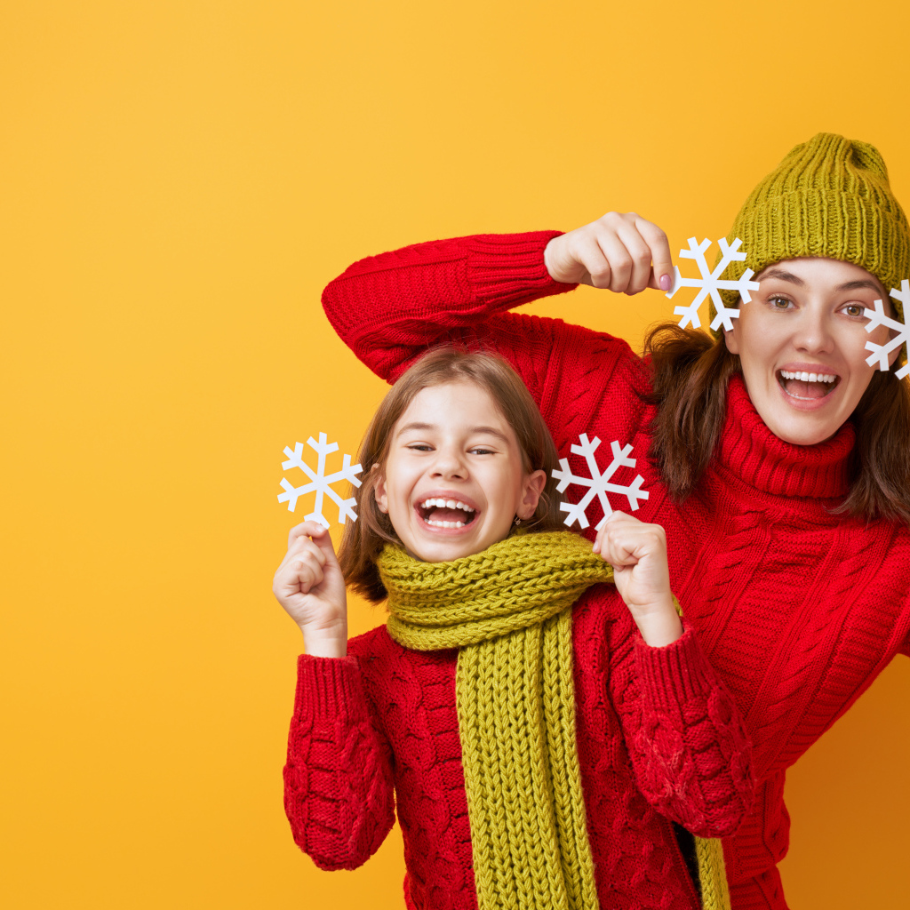 Веселые мама и дочка в красных свитерах на оранжевом фоне