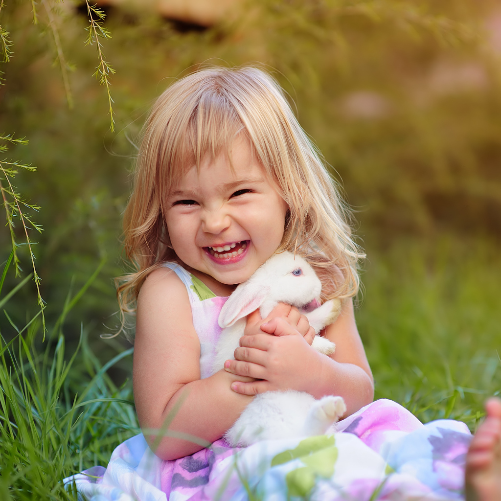 Довольная маленькая девочка обнимает белого кролика на траве 