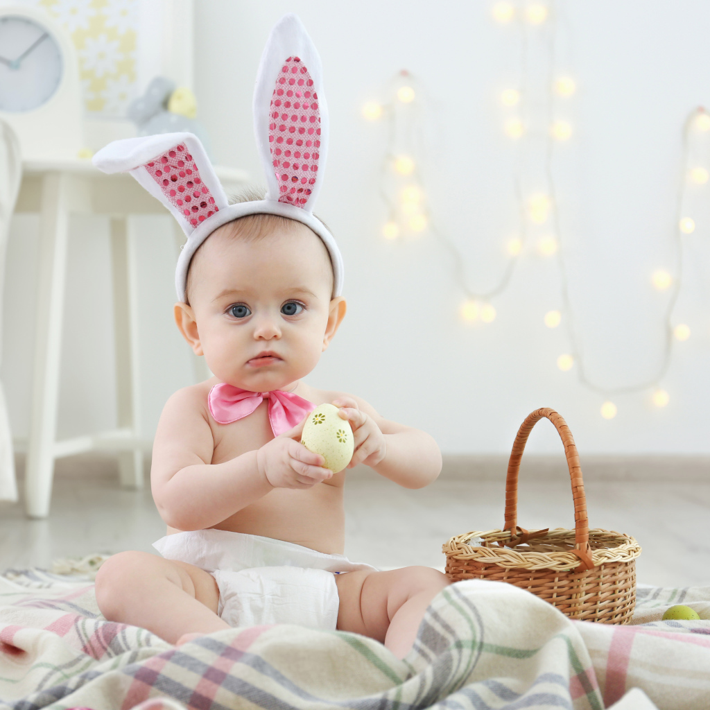 Милый ребенок с ушками на голове сидит пасхальными яйцами