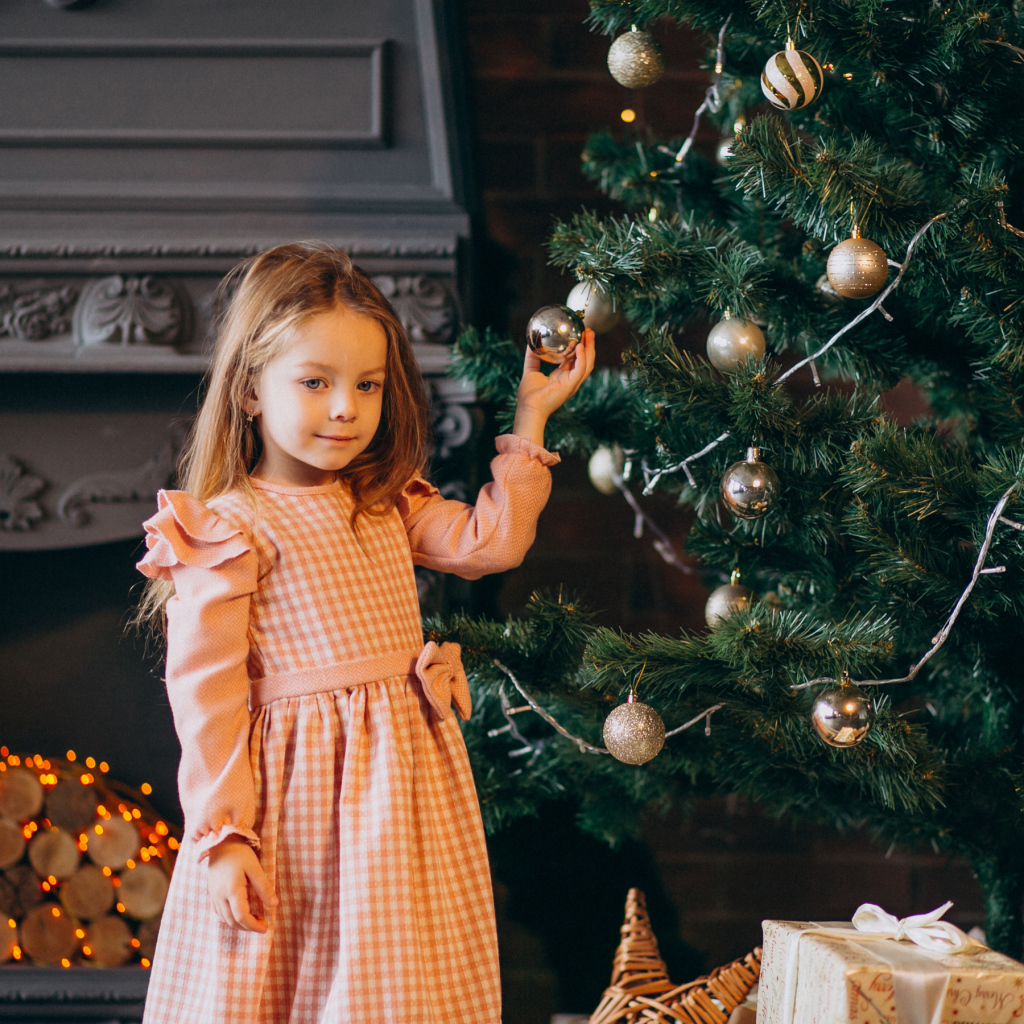 Милая маленькая девочка стоит у наряженной елки 