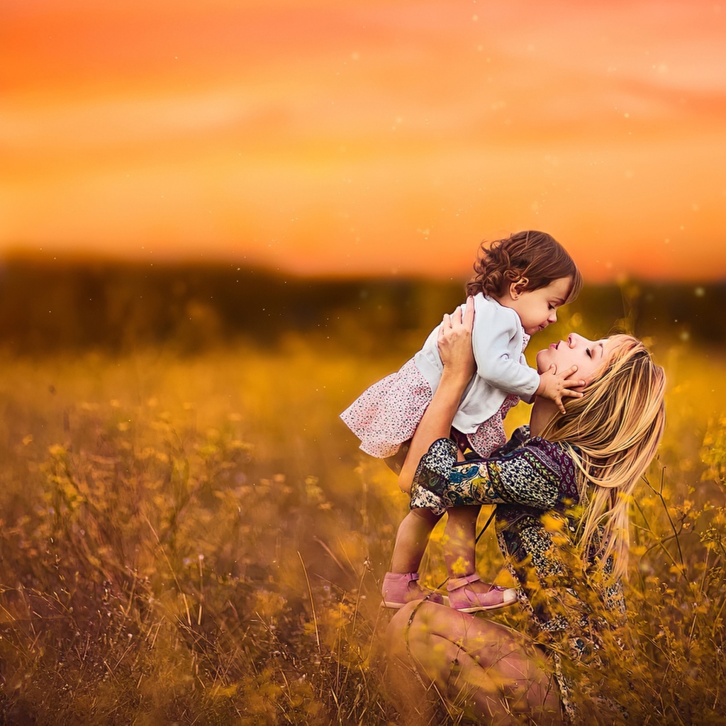 Девушка держит маленькую девочку на руках в поле на закате