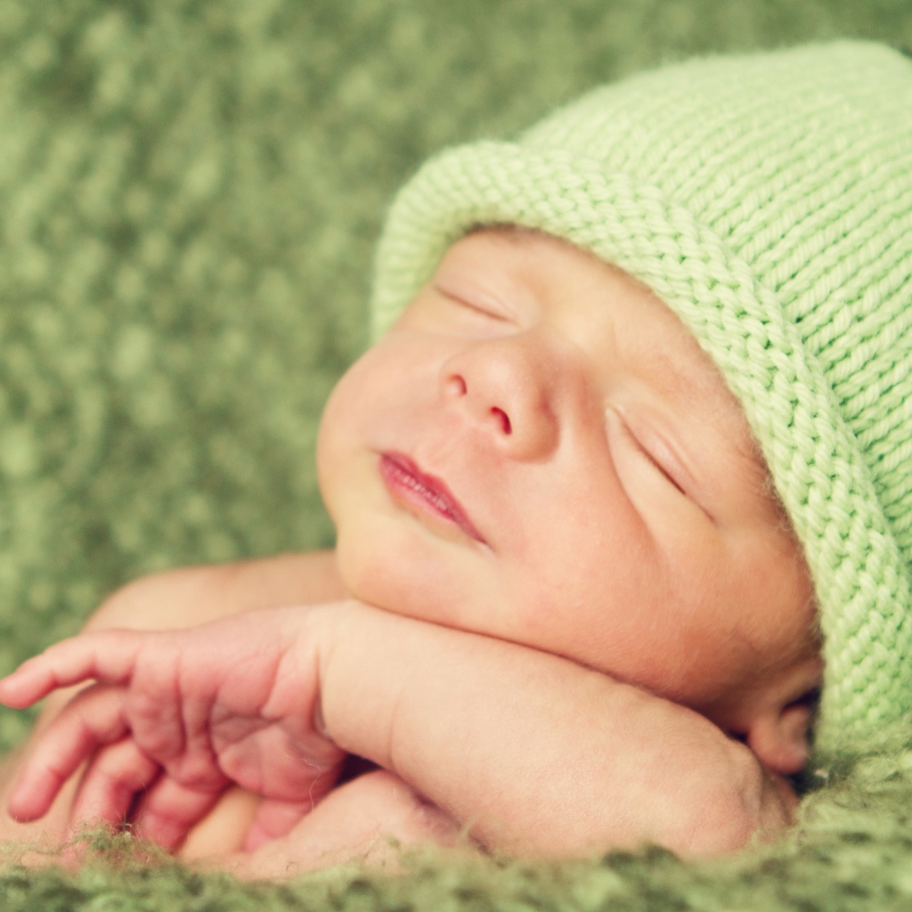 Зеленая вязаная шапка на голове у спящего ребенка 