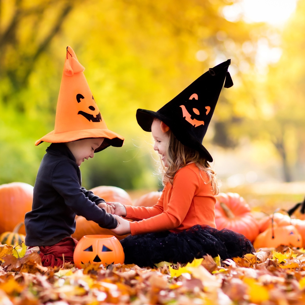 Маленькие мальчик и девочка в костюмах на Хэллоуин сидят на листве