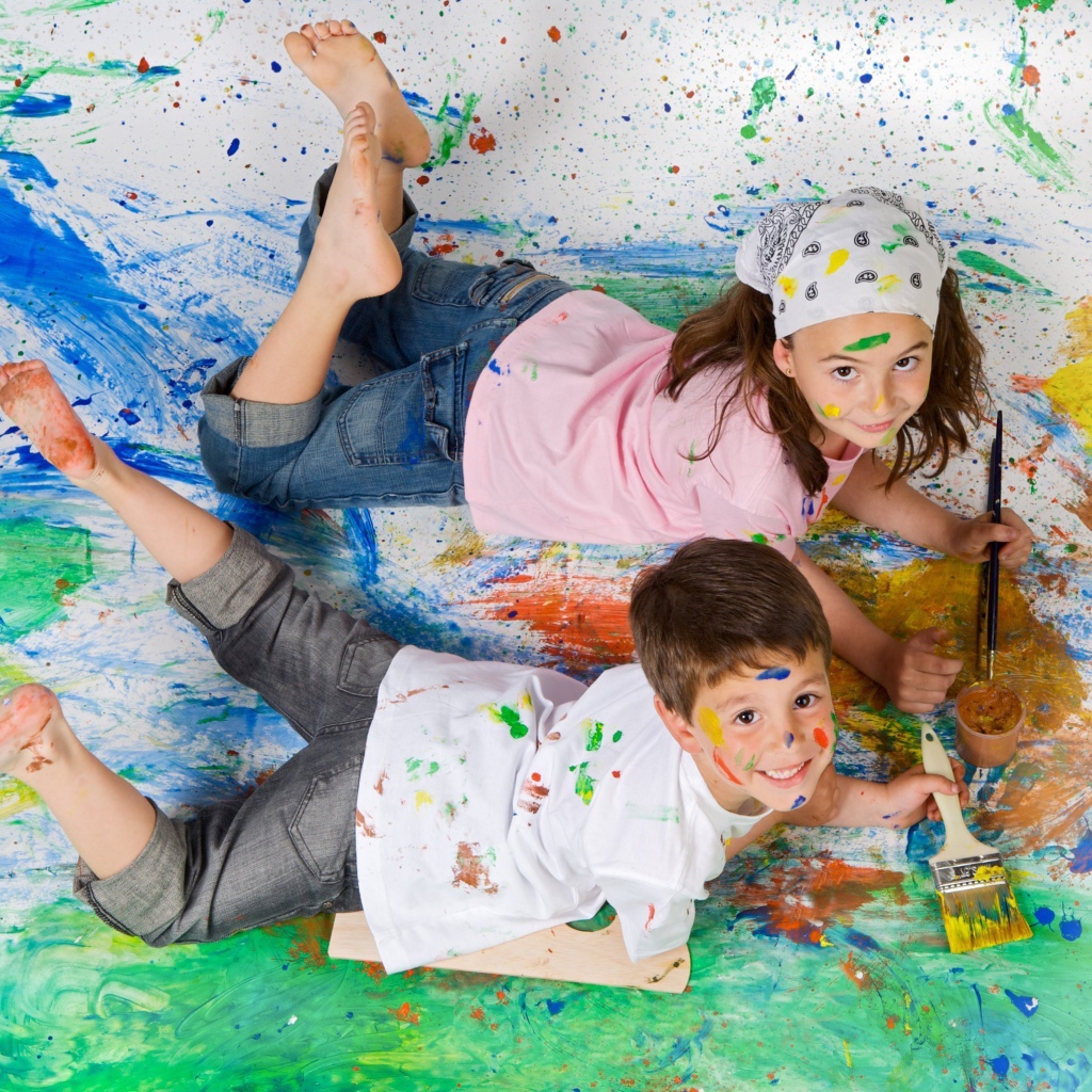 Маленькие мальчик и девочка рисуют красками на полу 