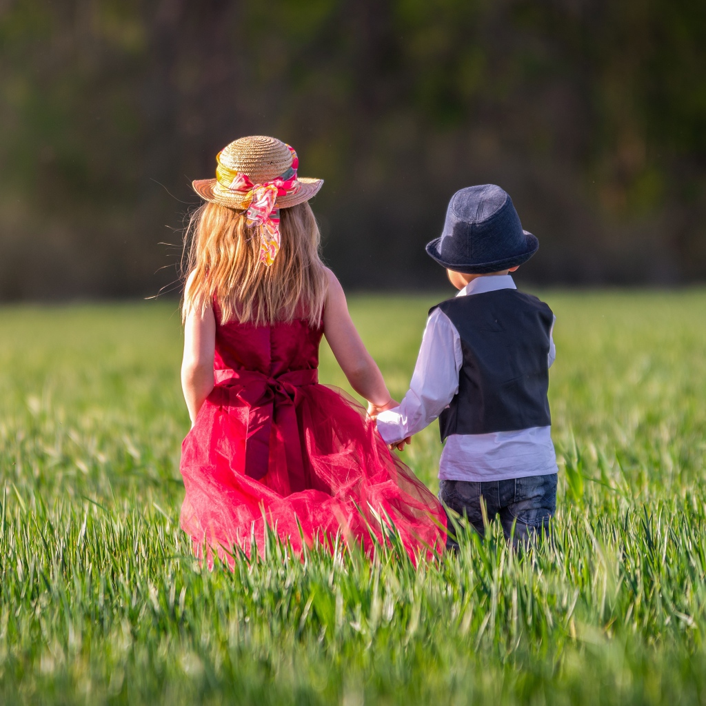 Маленькие мальчик и девочка идут по зеленому полю