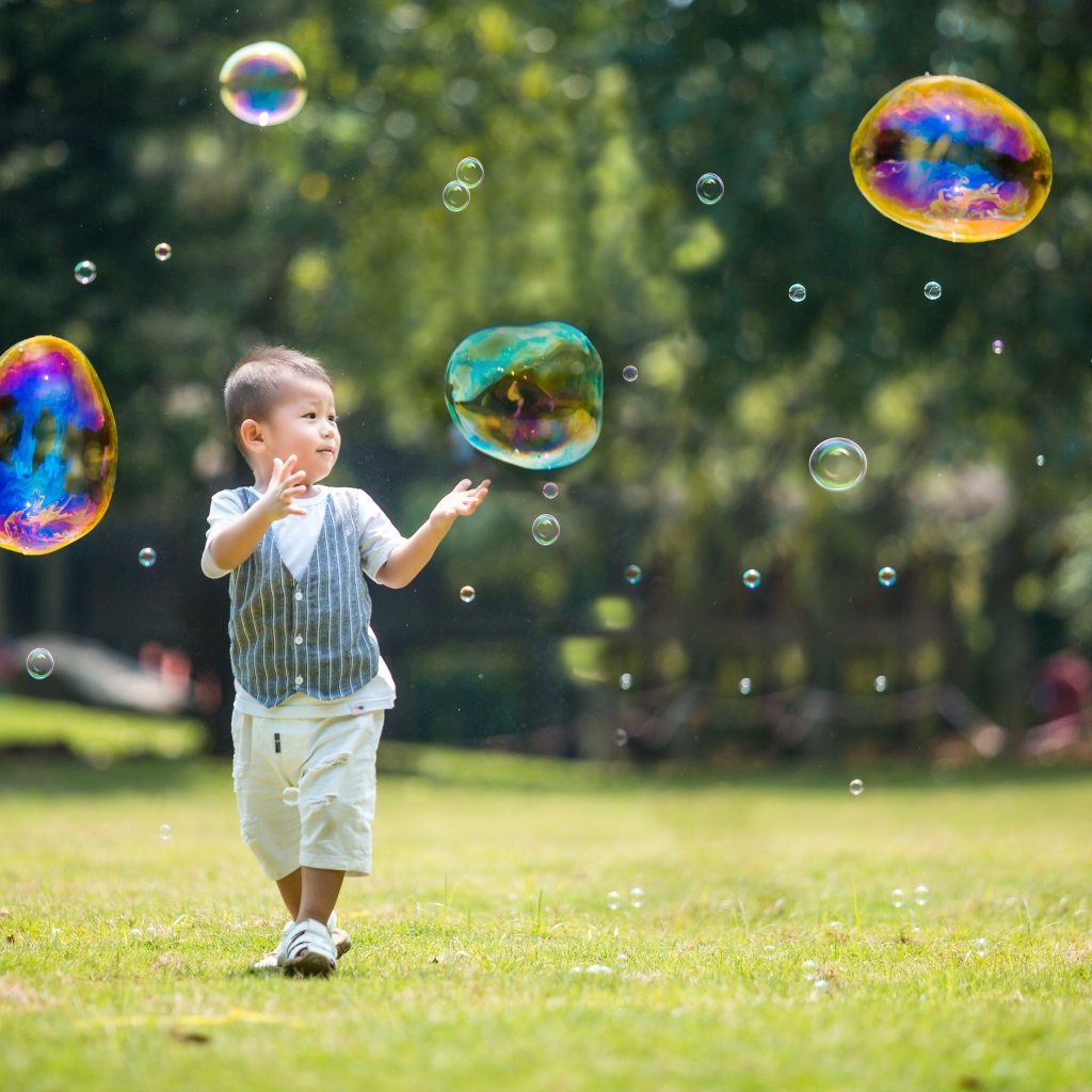 Маленький мальчик ловит мыльные пузыри