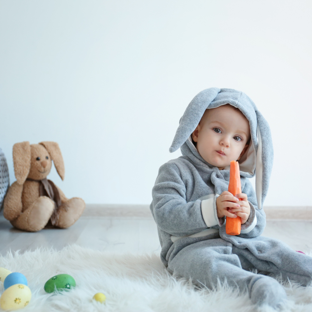 Маленький мальчик в костюме зайчика грызет морковь