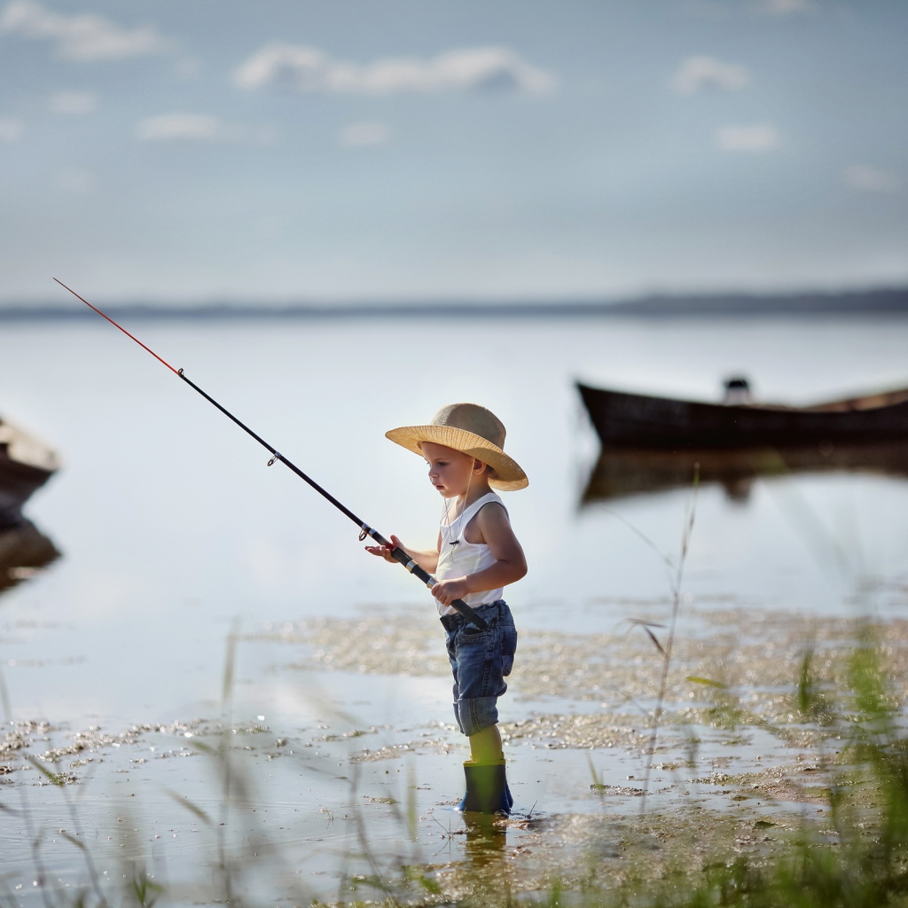 Маленький мальчик в шляпе ловит рыбу в озере 