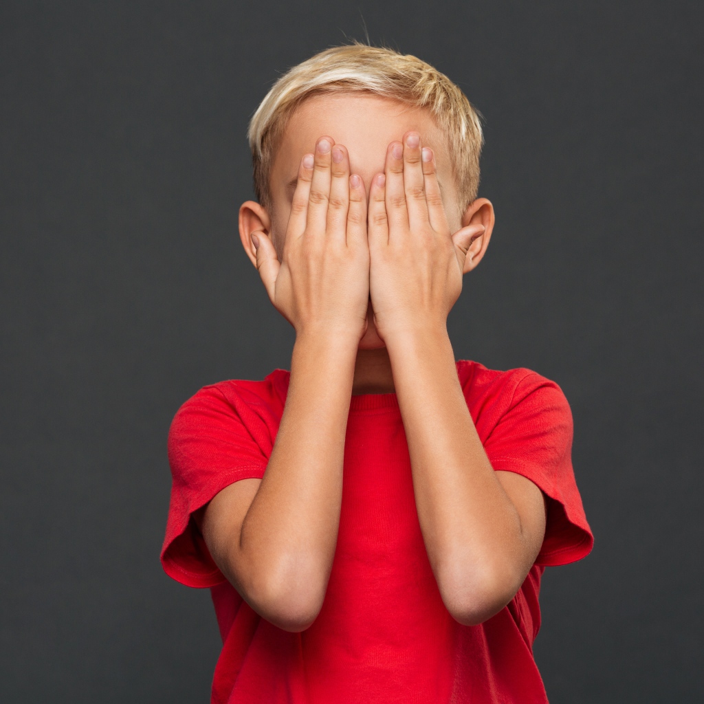 Маленький мальчик в красной футболке закрыл лицо руками 
