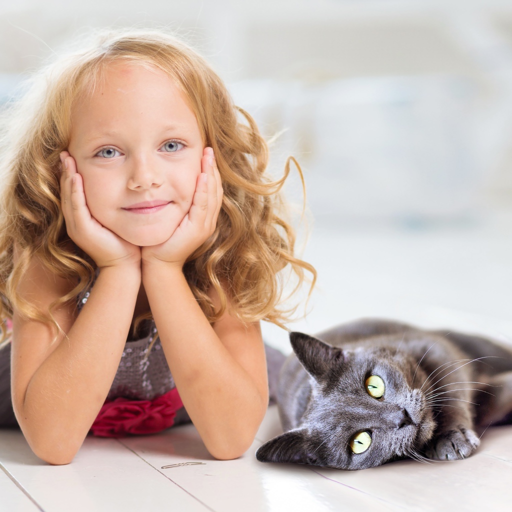 Маленькая милая голубоглазая девочка лежит на полу с котом