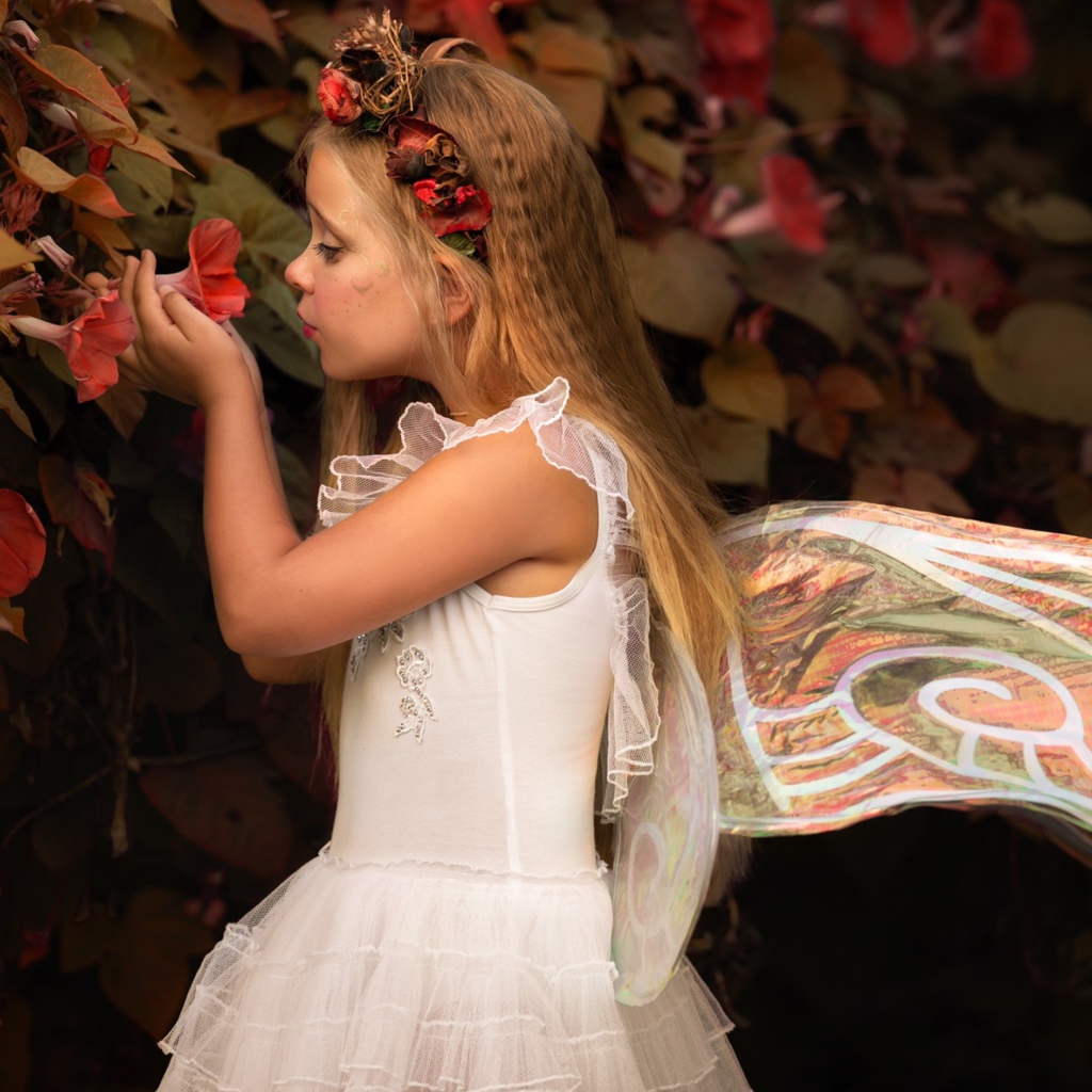 Маленькая девочка в костюме феи стоит у цветов