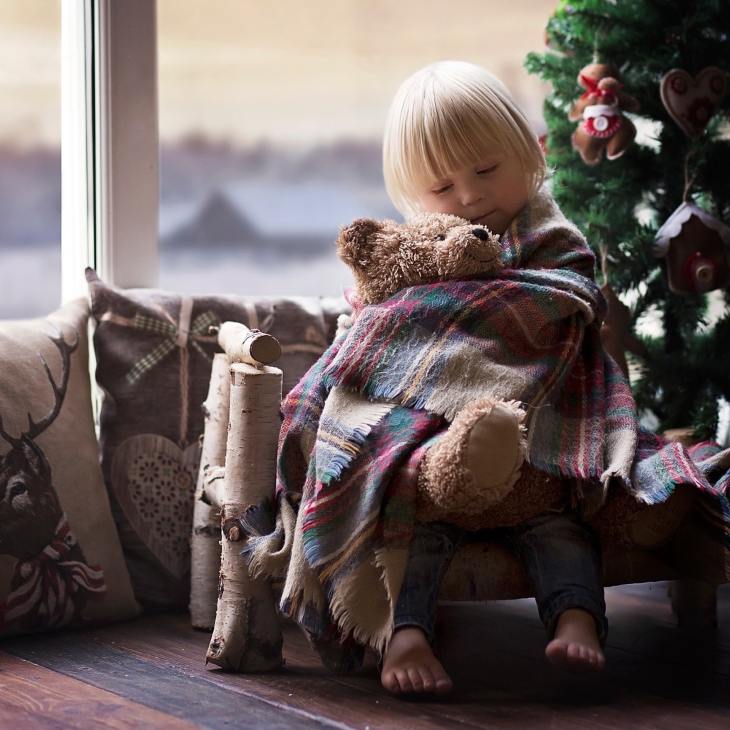 Маленькая девочка обнимает мишку у ели