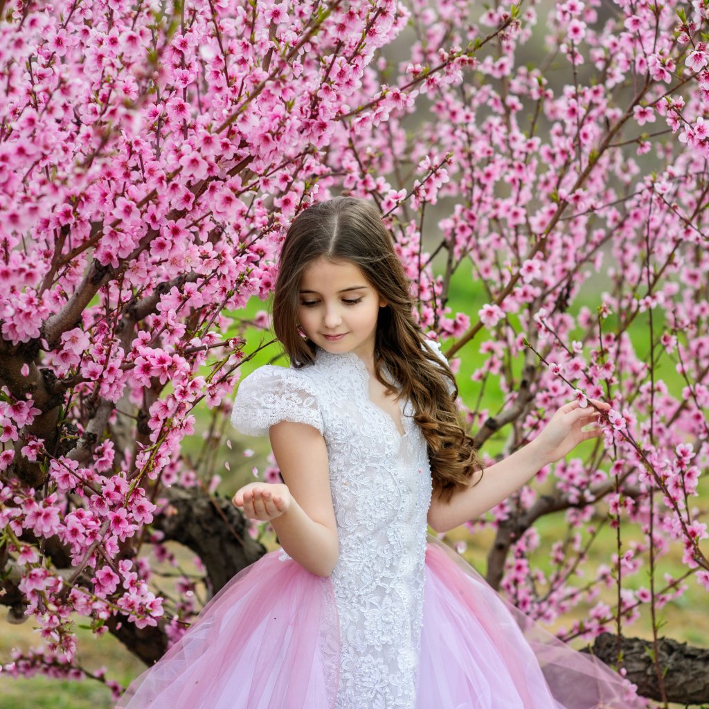 Маленькая девочка в красивом платье у дерева с розовыми цветами