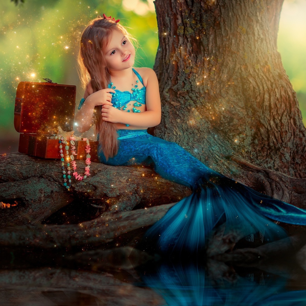 Маленькая девочка в костюме русалочки сидит у воды 