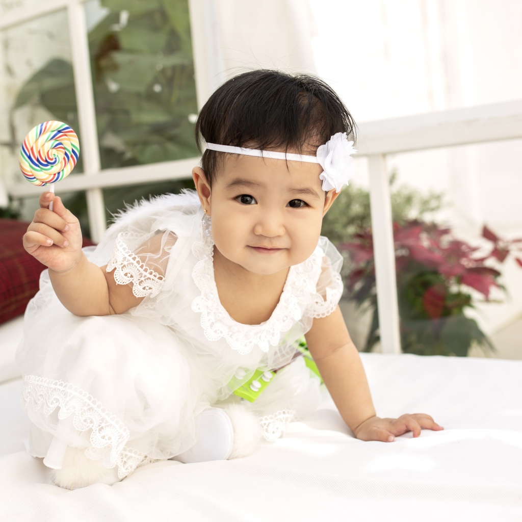 Маленькая девочка в белом платье с леденцом в руке