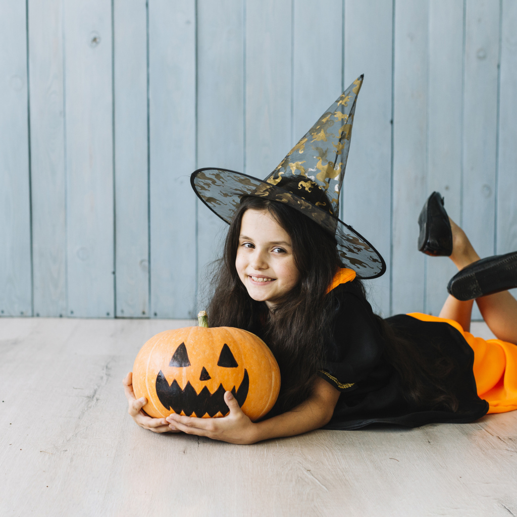 Маленькая девочка в костюме ведьмы с тыквой на Хэллоуин
