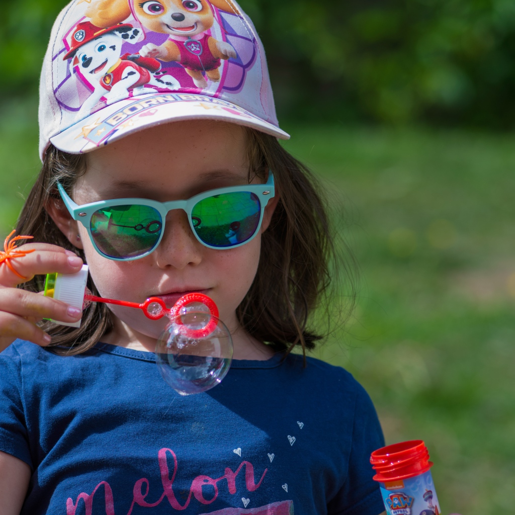 Маленькая девочка в очках с мыльными пузырями