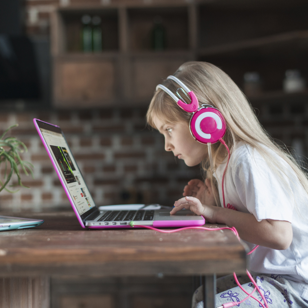 Маленькая девочка в наушниках сидит за ноутбуком