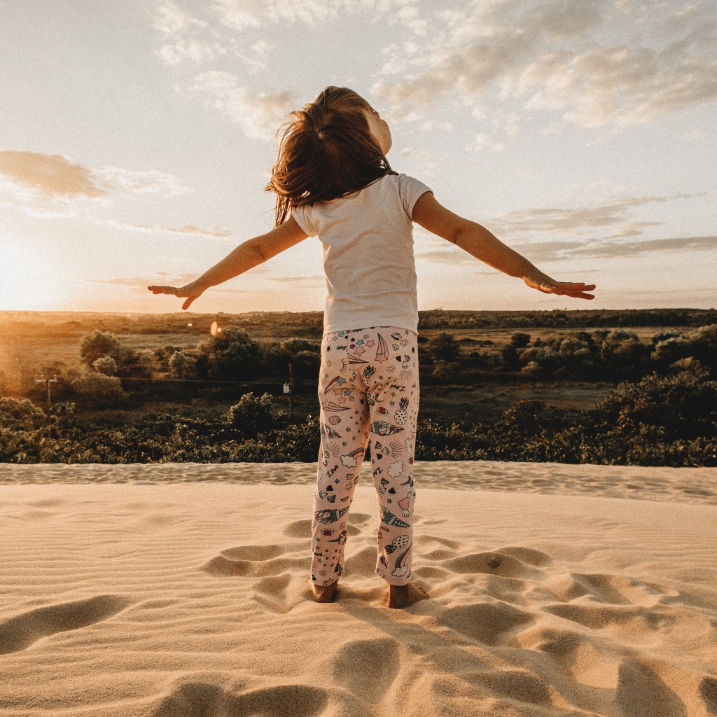 Маленькая девочка стоит на песку в лучах солнца