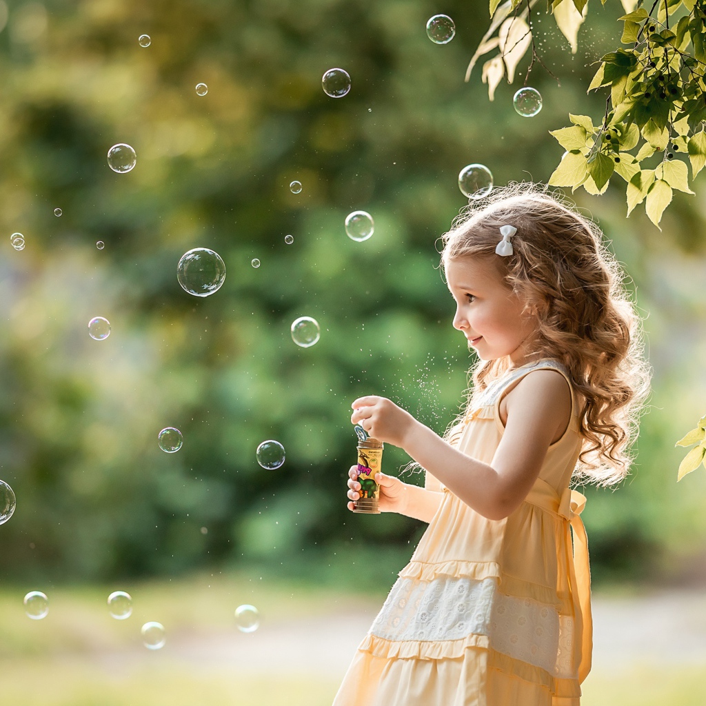 Маленькая девочка с мыльными пузырями в саду 