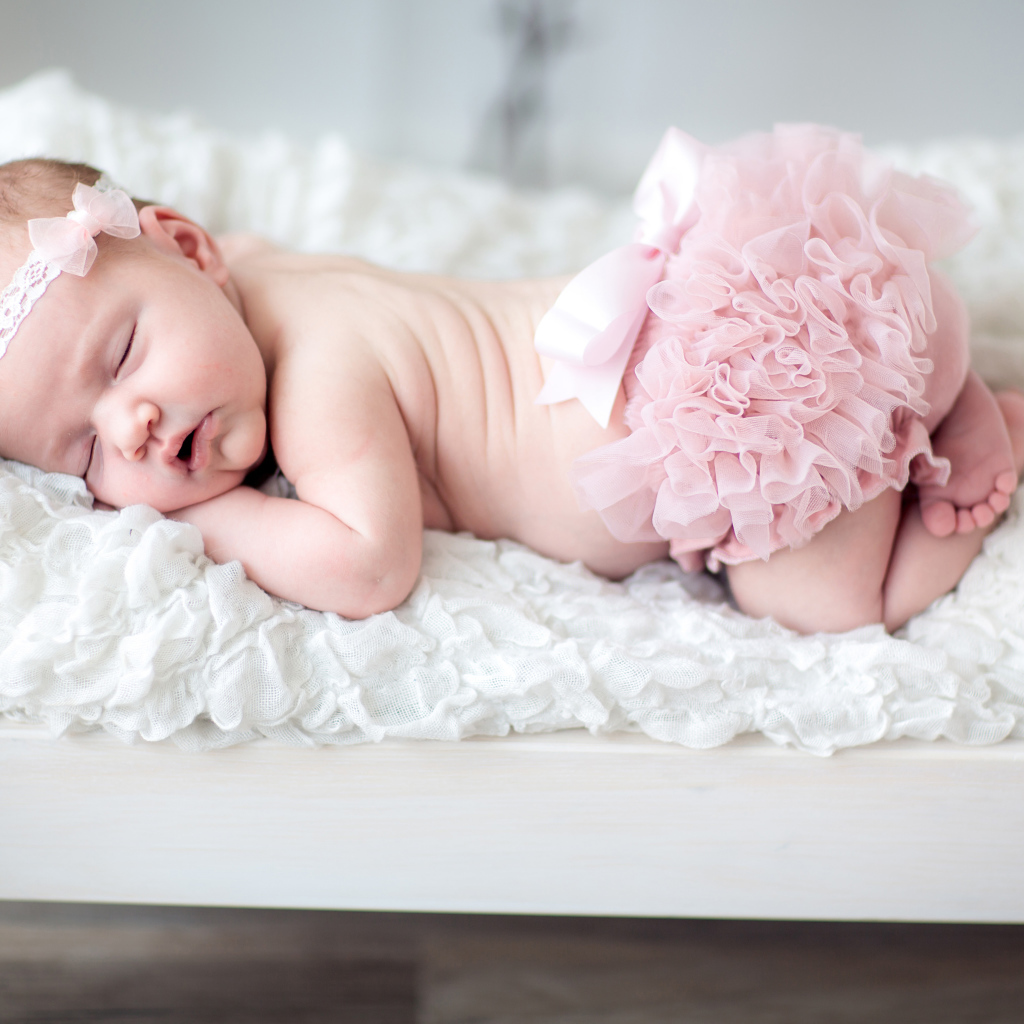 Маленькая спящая девочка в розовом костюме в кроватке