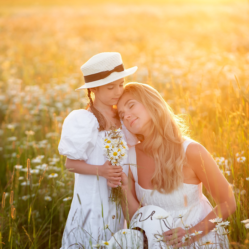 Мать с дочерью на поле с белыми ромашками в лучах солнца 