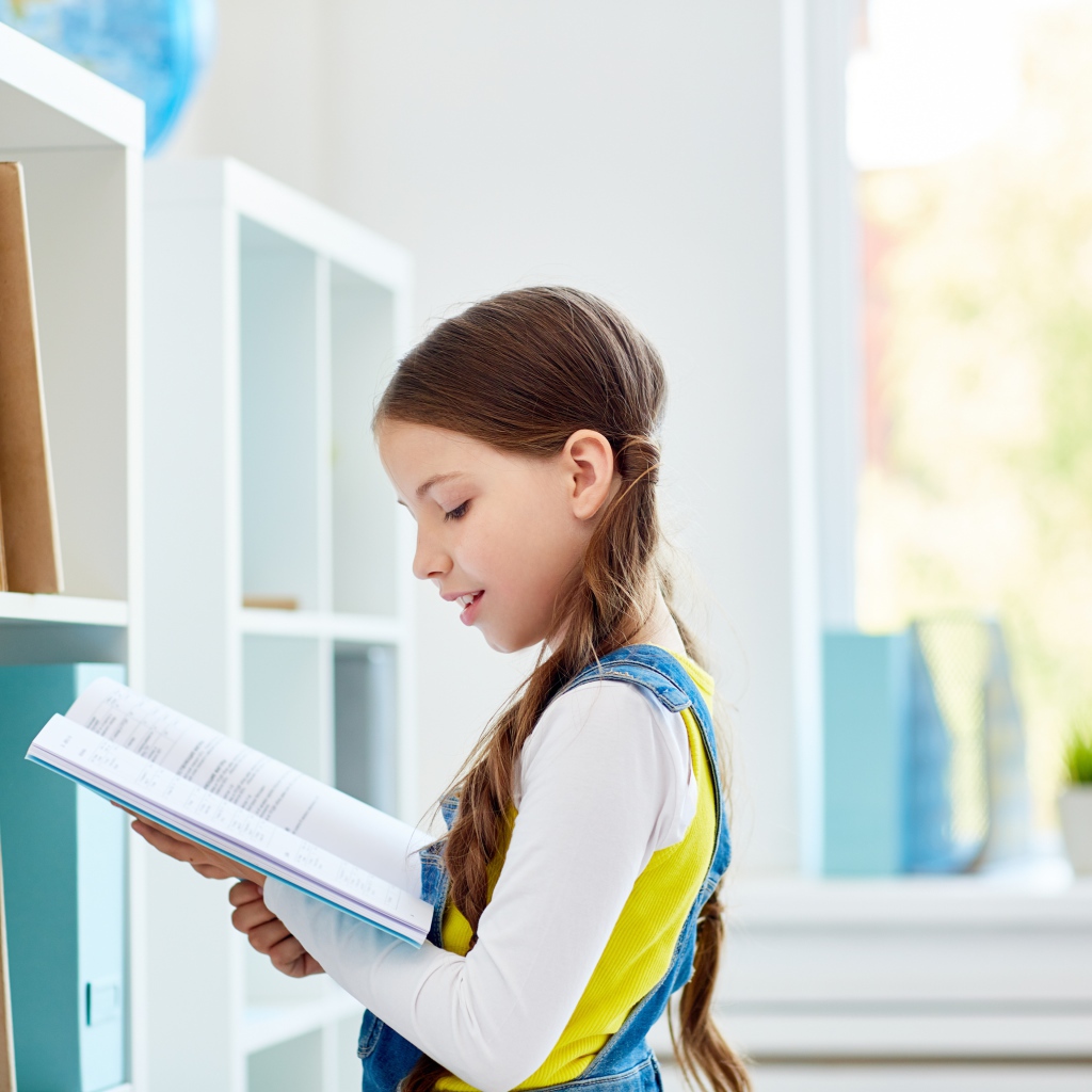 Умная девочка школьница с книгой в библиотеке 