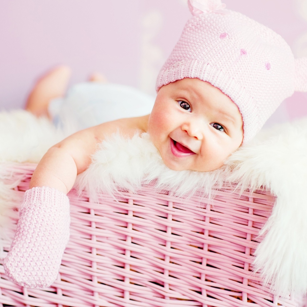 Улыбающийся грудной ребенок в шапке в розовой корзине 