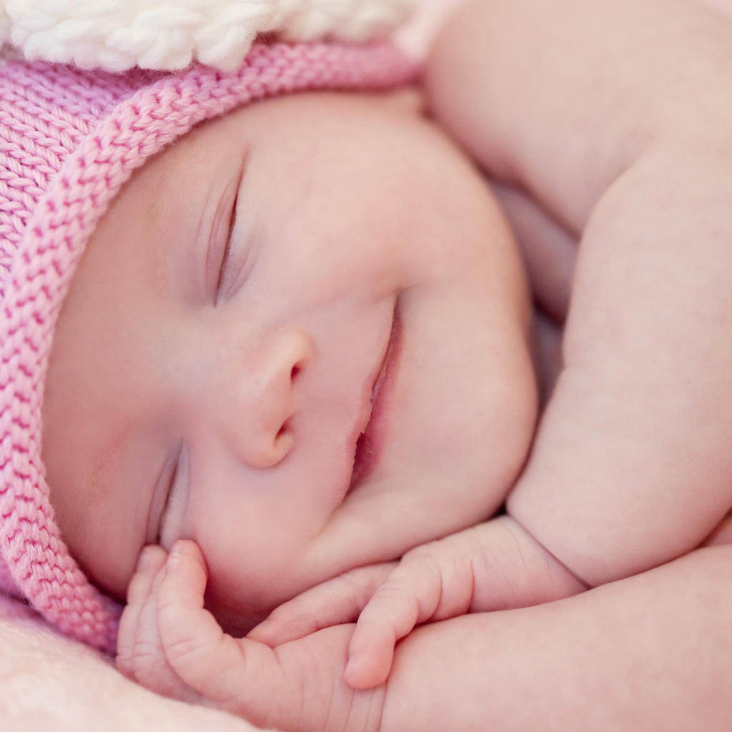 Улыбающийся грудной ребенок в розовой вязаной шапке 