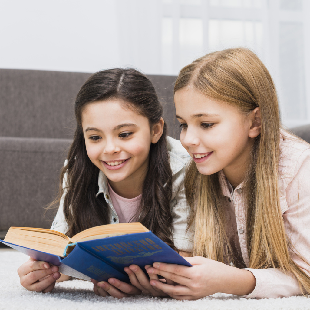 Две маленькие девочки читают книгу на полу