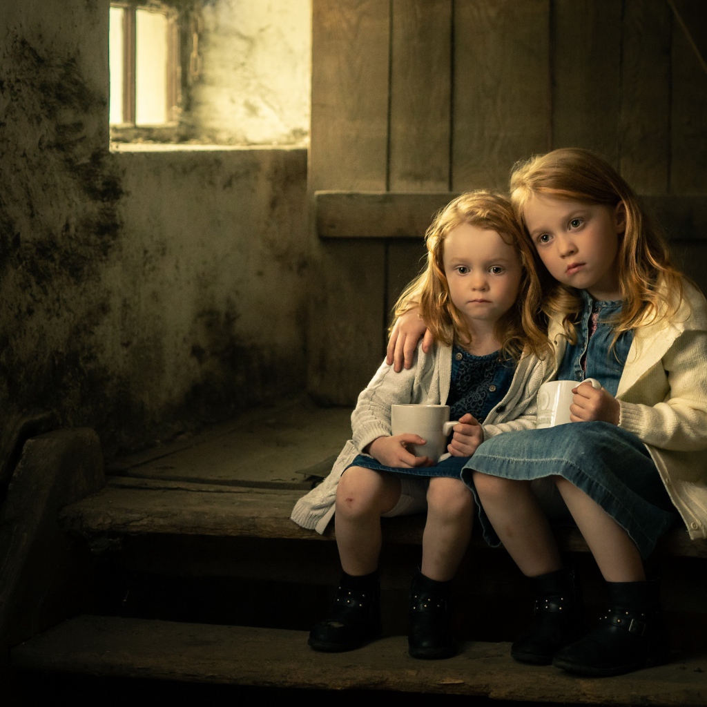 Две маленькие сестры пьют какао на ступеньках дома