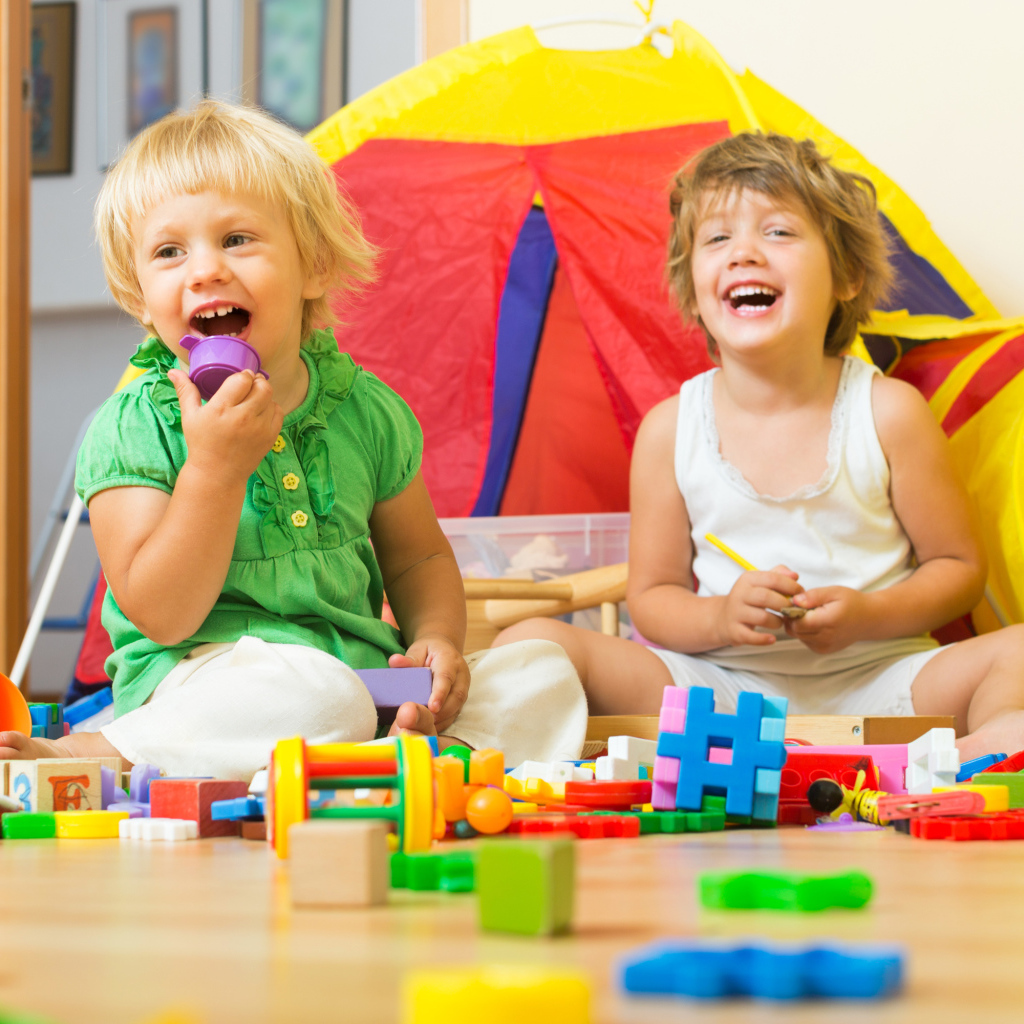 Два улыбающихся ребенка играют с конструктором 