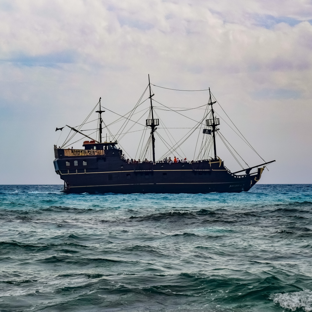 Large black pirate ship with lowered sails at sea