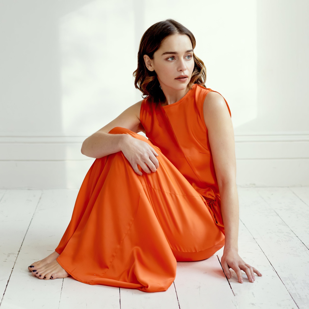 Актриса Эмилия Кларк  в оранжевом платье сидит на полу