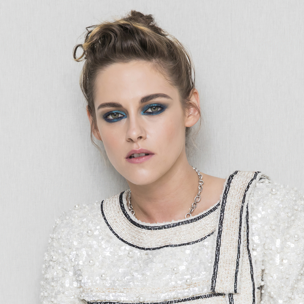 Актриса Кристен Стюарт с накрашенными глазами на фоне серой стены 