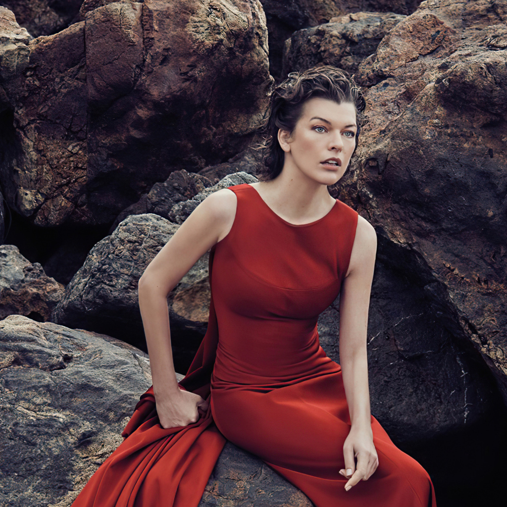Актриса Милла Йовович в красном платье сидит на камне