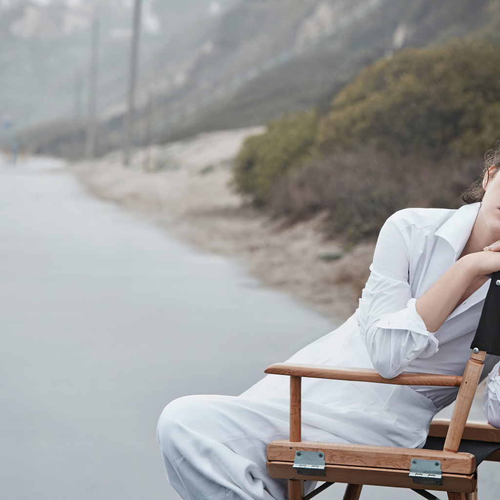 Актриса Милла Йовович в белом платье сидит на стуле