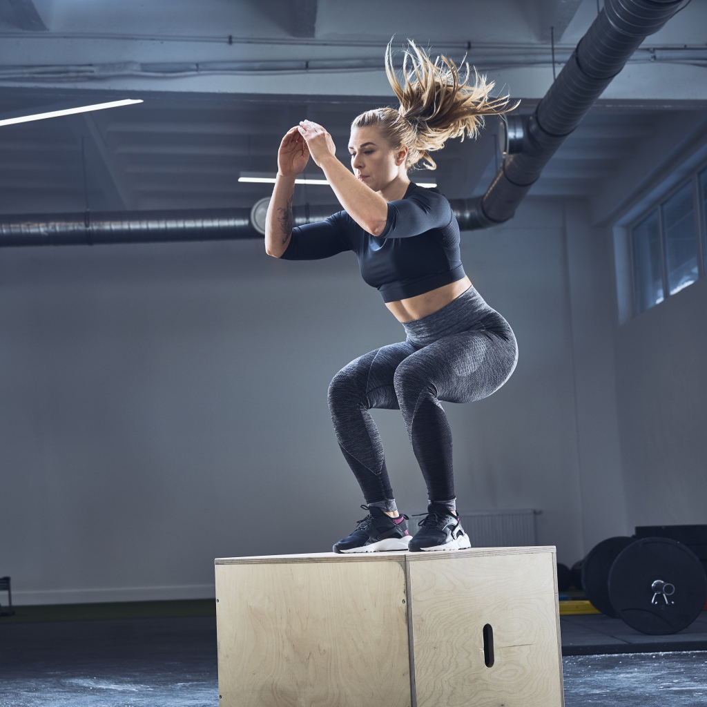 Спортивная девушка запрыгивает на тумбу в спортзале 