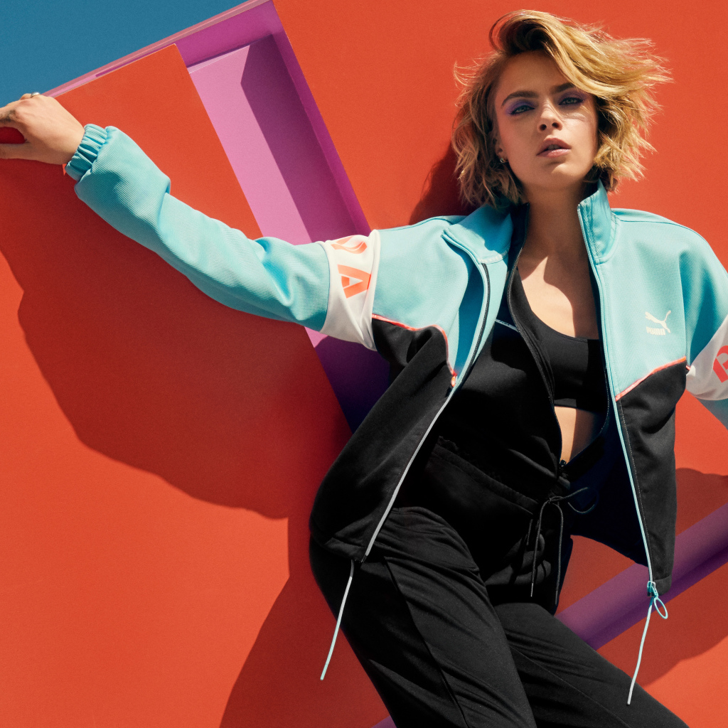 Красивая актриса Кара Делевинь в спортивном костюме у стены 