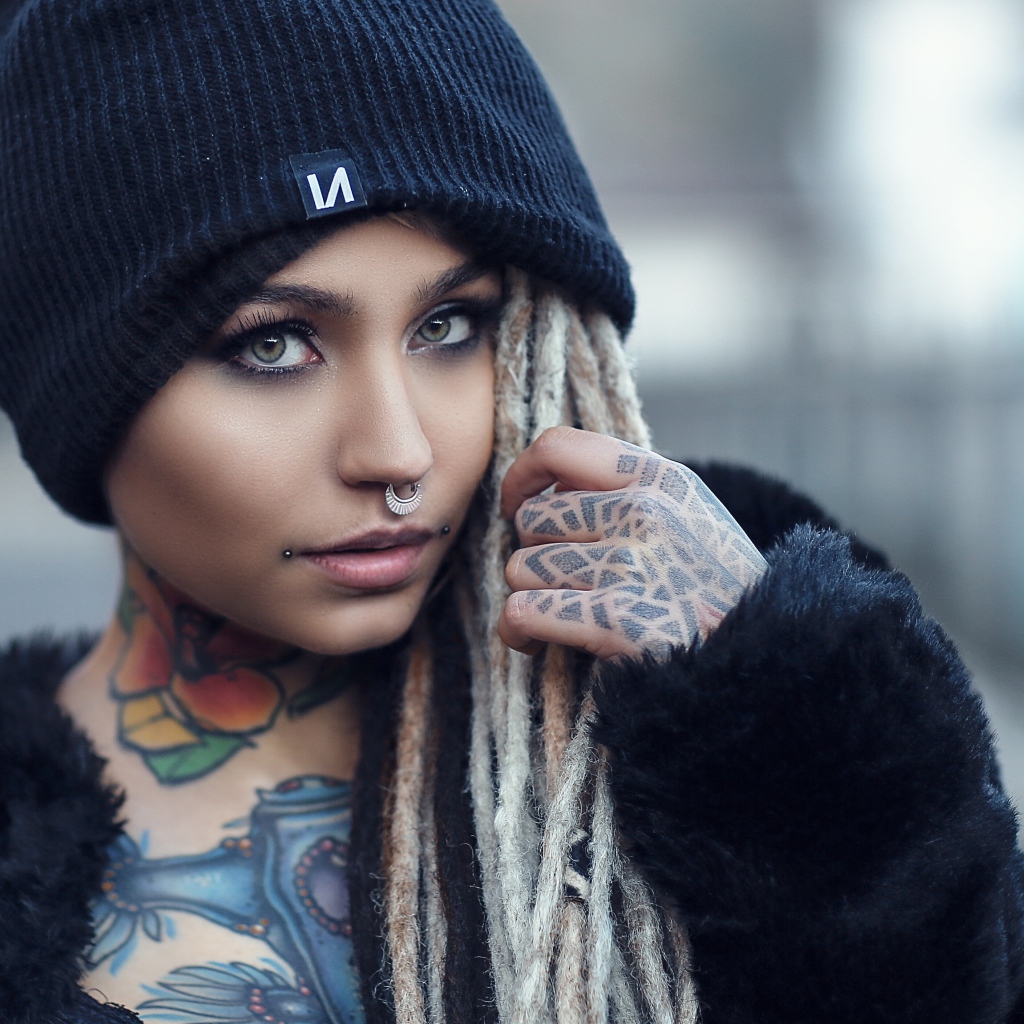 Красивая девушка в черной шапке с татуировками на теле 