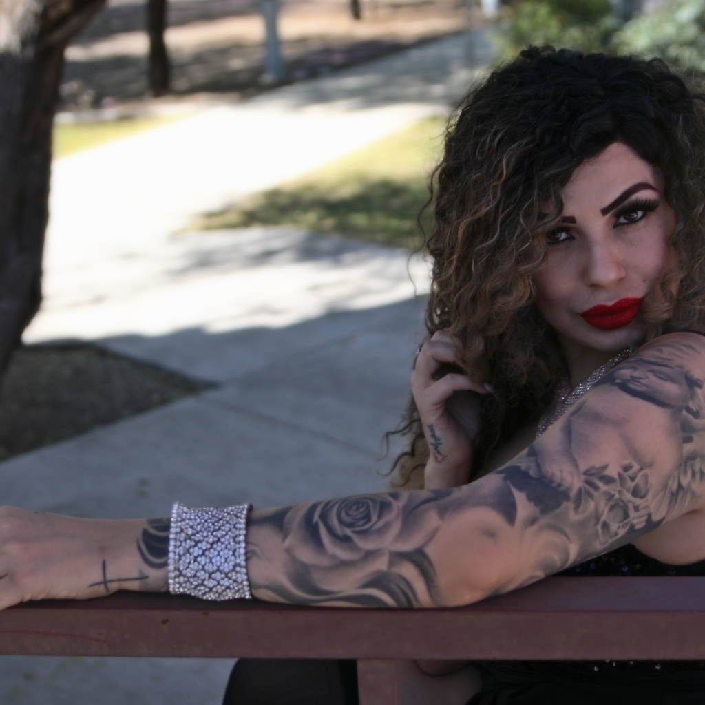 Красивая девушка с татуировками на руках сидит на лавке 