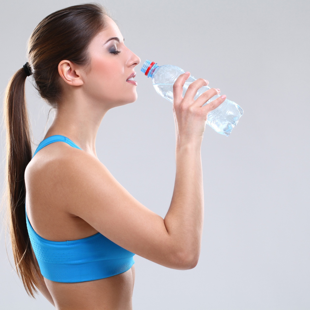 Красивая спортивная девушка пьет воду на сером фоне 