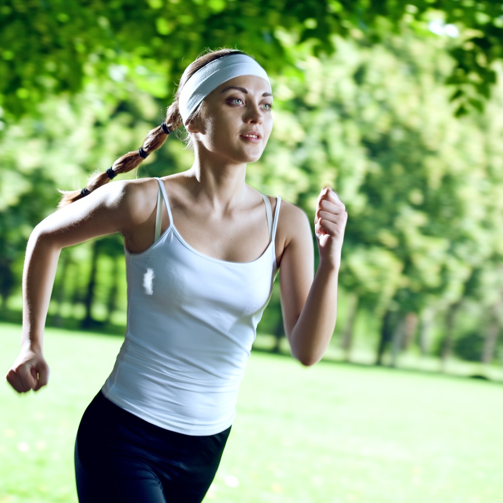 Девушка спортсменка в белой майке занимается бегом