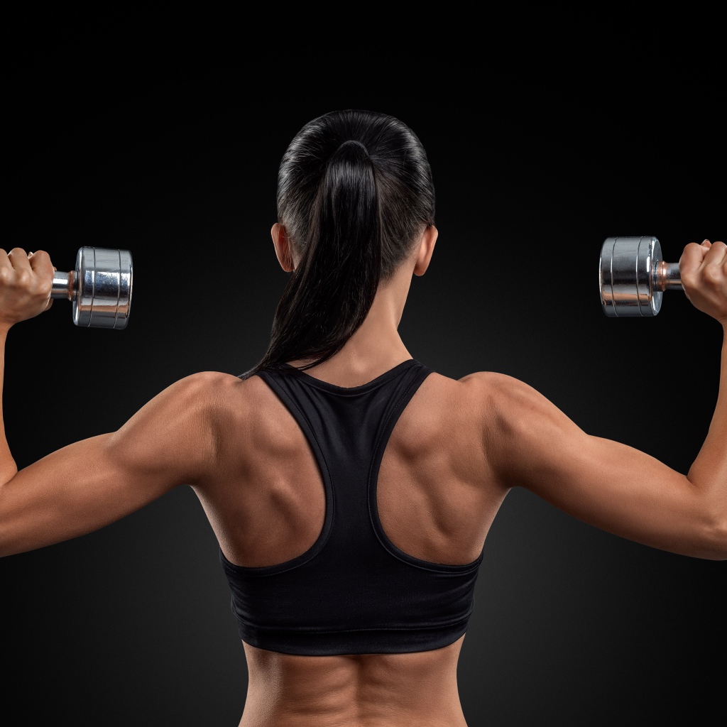 Стройная спортивная девушка с гантелями в руках на черном фоне